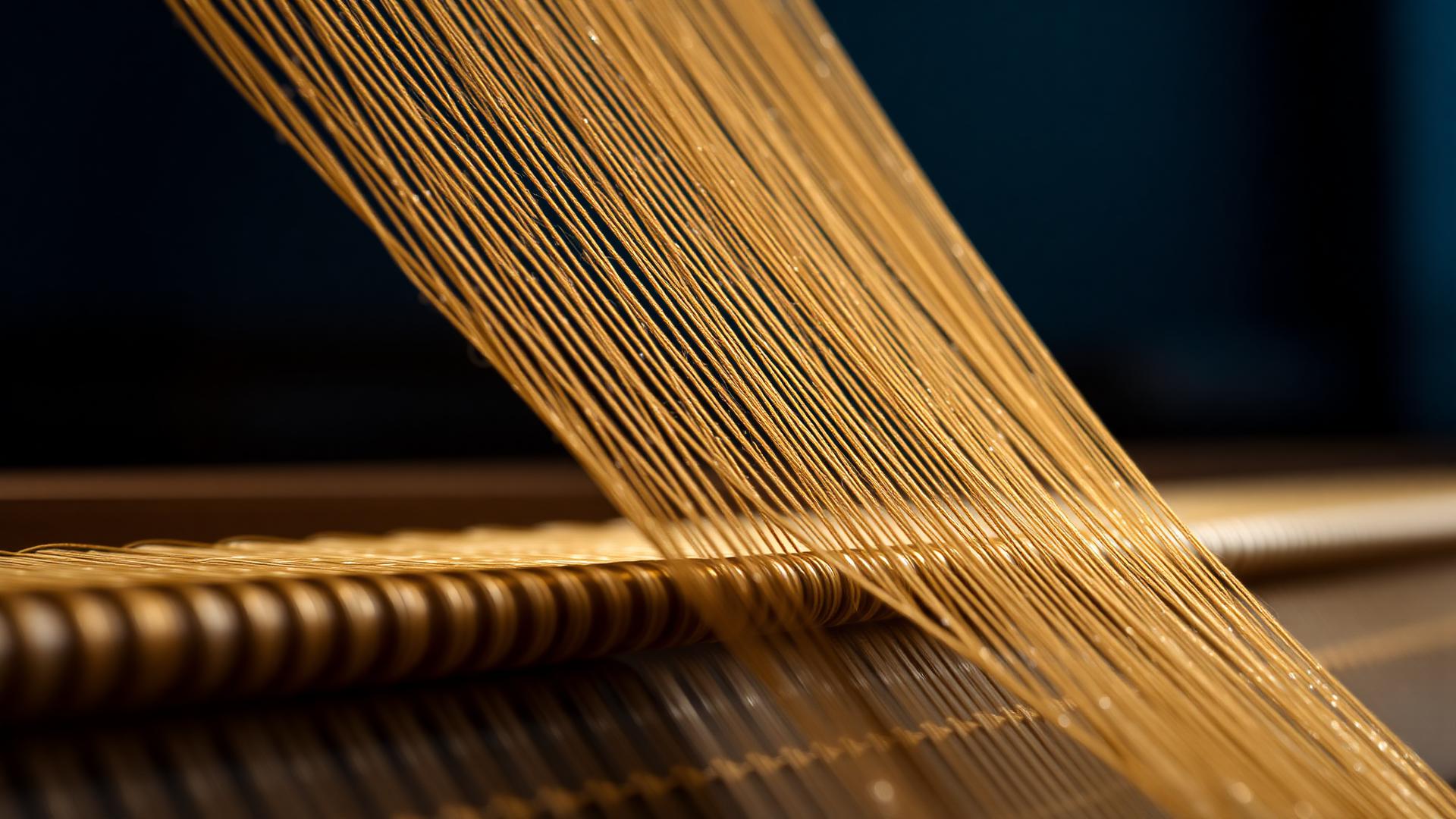 Gold weft threads passing through a navy warp on a loom